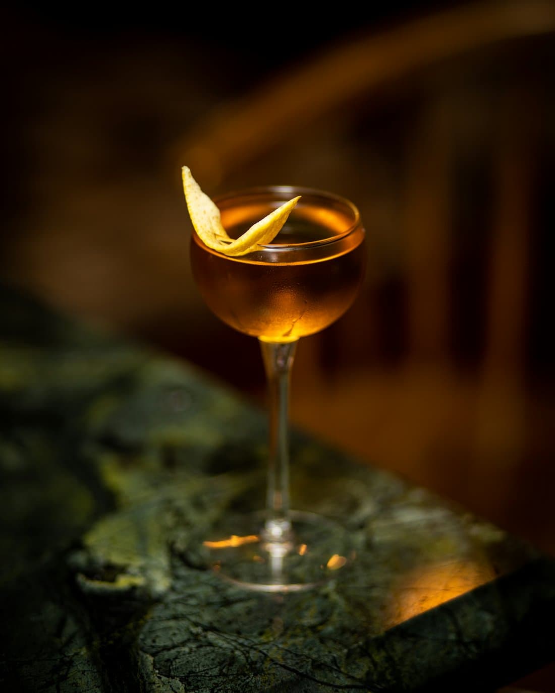 Cocktail ambré au zeste d'orange dans une coupe, lumière tamisée