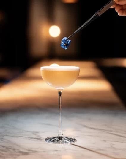 Fleur déposée à la pince sur un cocktail en coupe, bar en marbre